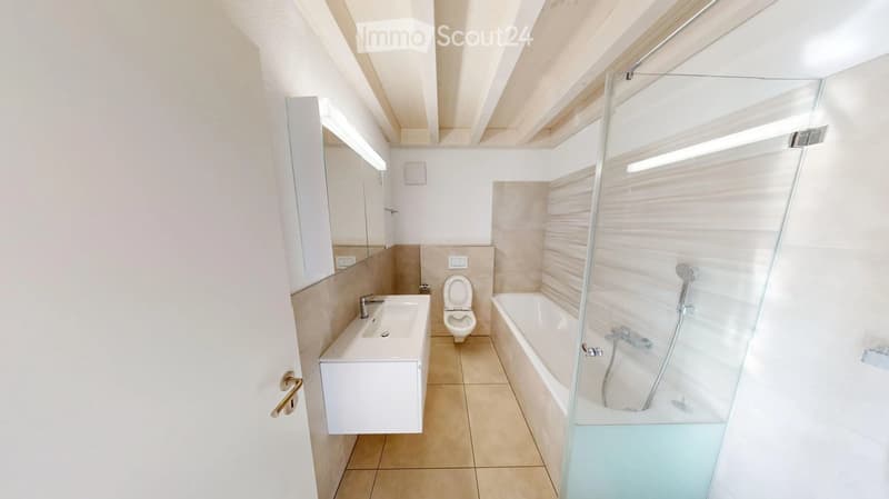 Modern bathroom with a white sink, toilet, bathtub, and glass-enclosed shower. Light-colored tiles and a sleek design.