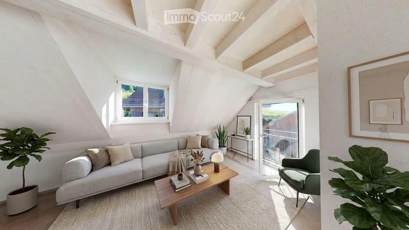 Bright living room with white walls, wooden ceiling beams, large windows, and a sliding glass door leading to a balcony. Features a grey sectional sofa, wooden coffee table, side table, green armchair, and decorative plants.