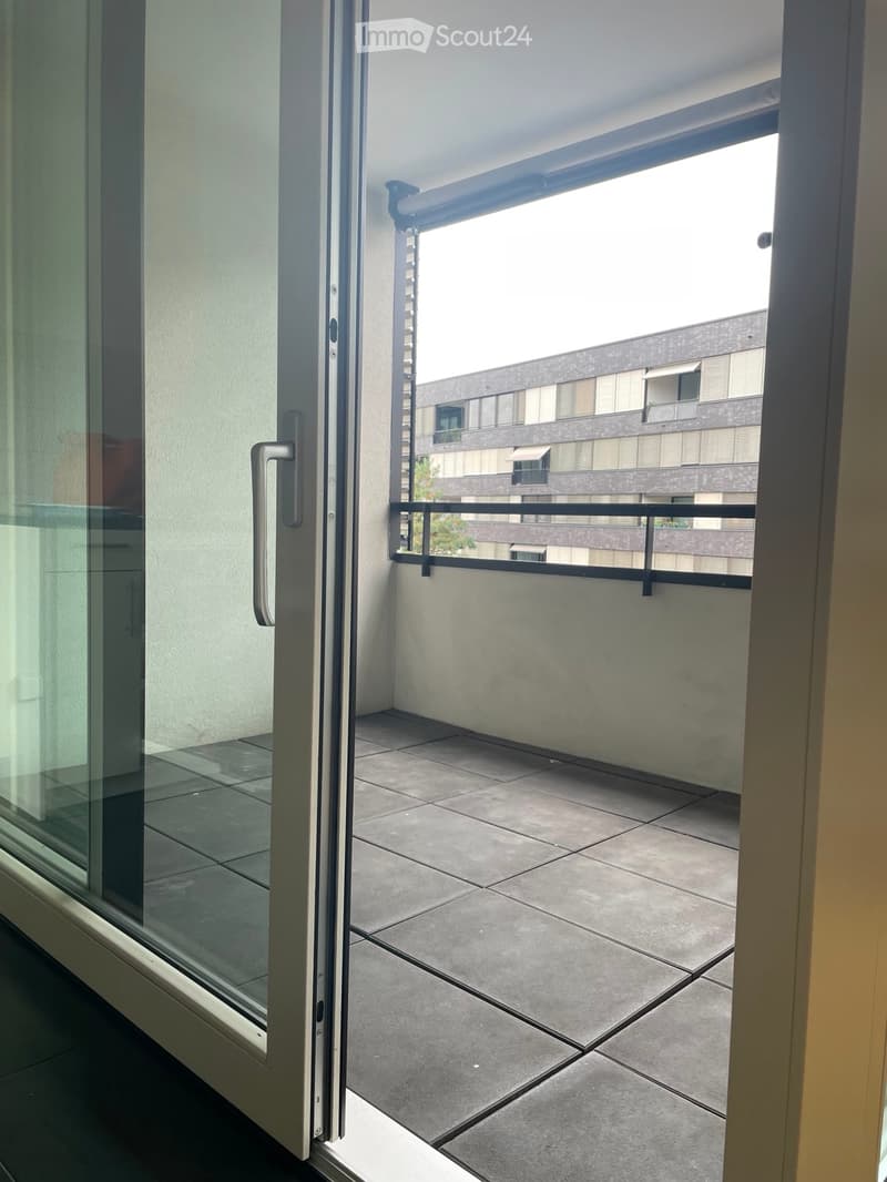 Balcony with tiled floor, metal railing, and glass sliding door leading to the interior.