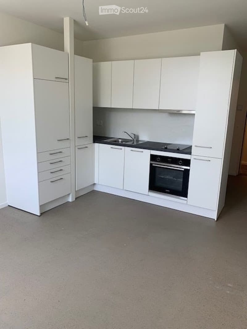 Modern, minimalist kitchen with white cabinets, a sink, a stove, and an oven. The space is clean and uncluttered, featuring a grey floor and neutral color scheme.