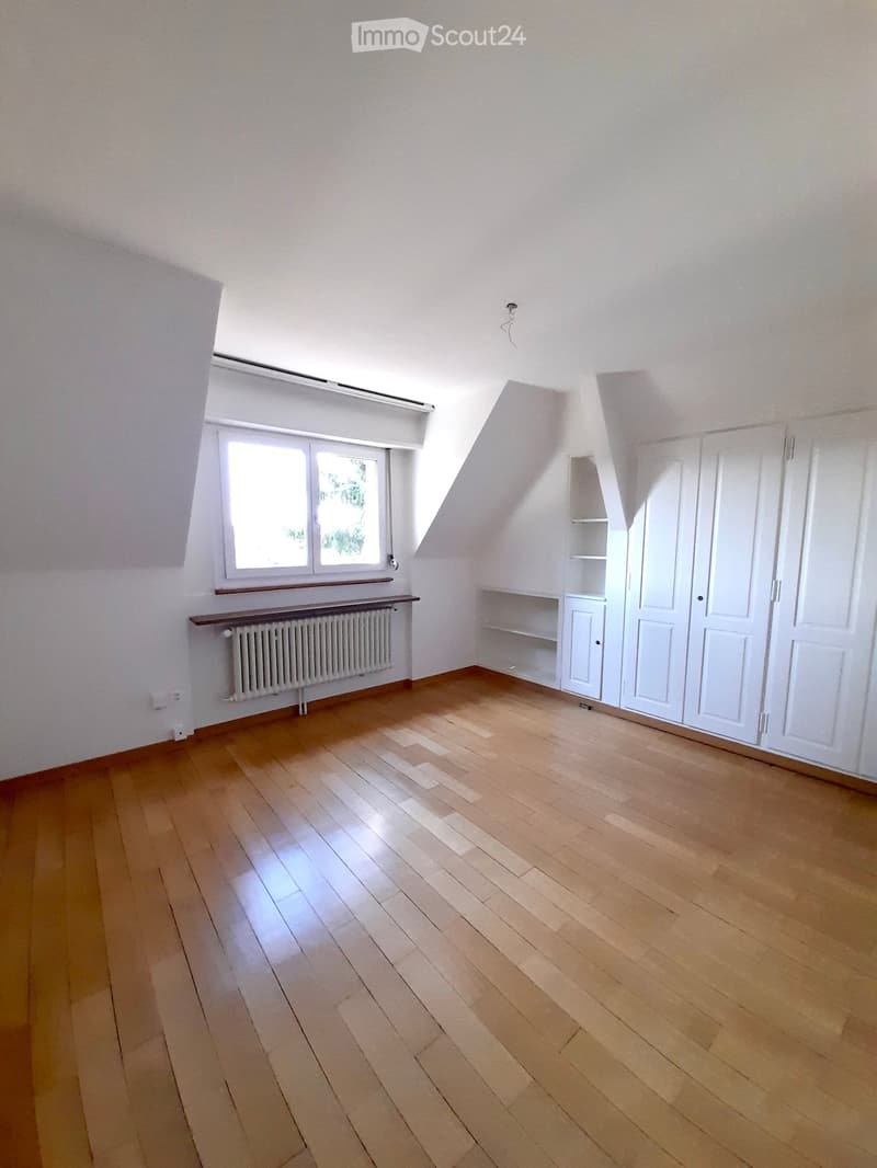 Empty attic room with wooden flooring, white walls, a window, built-in closet, and radiator.