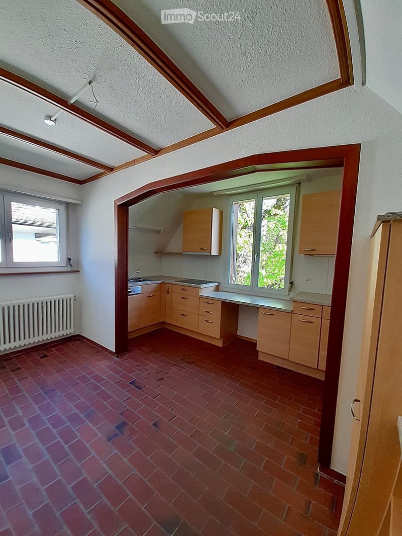 Empty kitchen with wooden cabinets, a sink, and a radiator, featuring a red tiled floor and white walls.