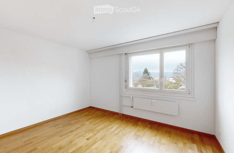 Empty room with wooden flooring, white walls, and a large window offering a view of the landscape.
