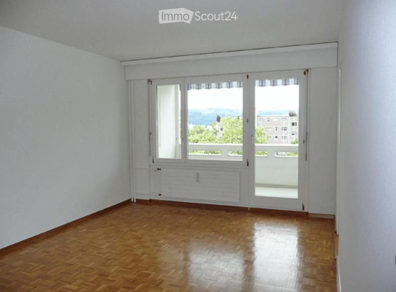 Empty room with wooden flooring, white walls, large windows, and a view of the outdoors.