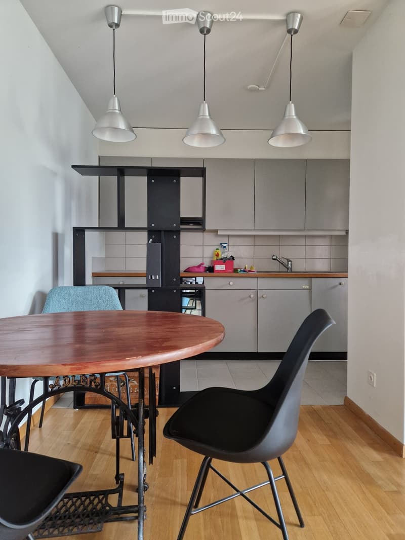 Modern kitchen with grey cabinets, wooden floor, round wooden table, black chairs, and pendant lights.
