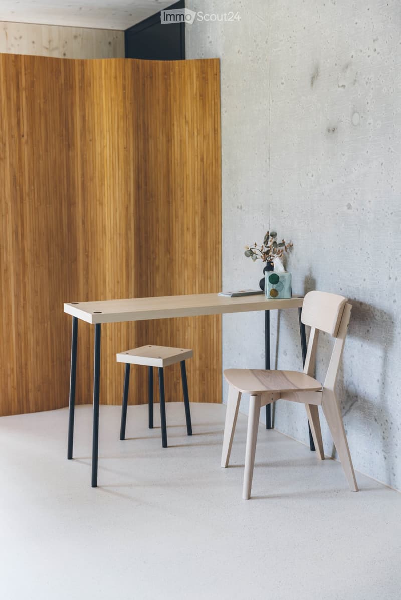Minimalist room with a light wooden table, two chairs, a small stool, and a vase with dried flowers on the table.