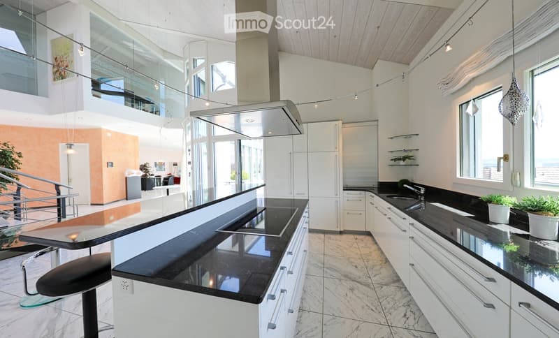 Modern kitchen with white cabinets, black countertops, and a central island with a built-in sink and stove. Features a sleek design with pendant lighting and a view of an adjacent living area.