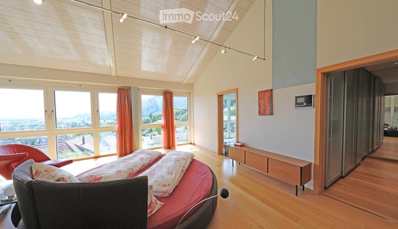 Bright living room with large windows offering a scenic view, featuring a red sofa, a wicker chair, and a small wooden table.