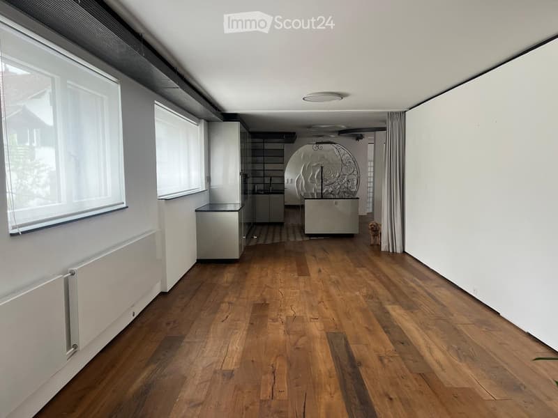 Empty room with wooden flooring, white walls, large windows with blinds, and a radiator on the left side.
