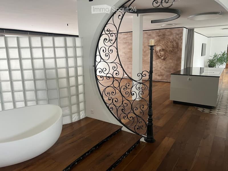 Modern bathroom with a freestanding bathtub, wooden flooring, a decorative candle on a stand, a mirror, and a plant in the background.