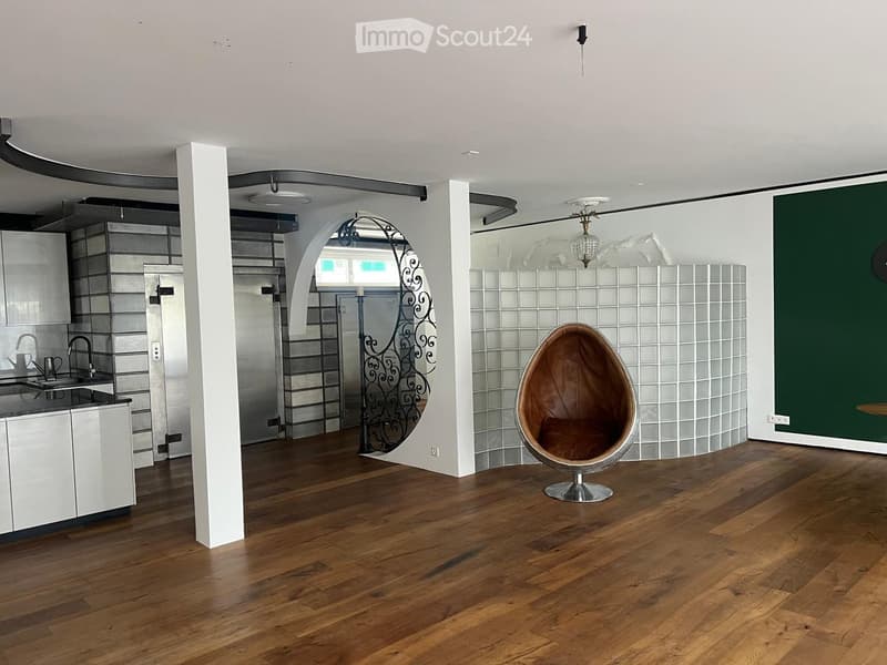 Open-plan living and kitchen area with wooden flooring, white kitchen cabinets, a modern sink, and a distinctive egg-shaped chair.
