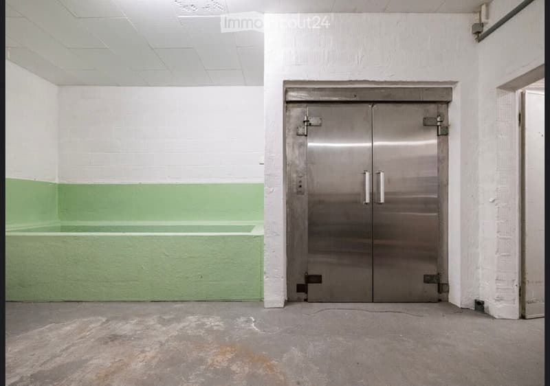 Empty room with white and green painted walls, a concrete floor, and a large metal door with silver handles.