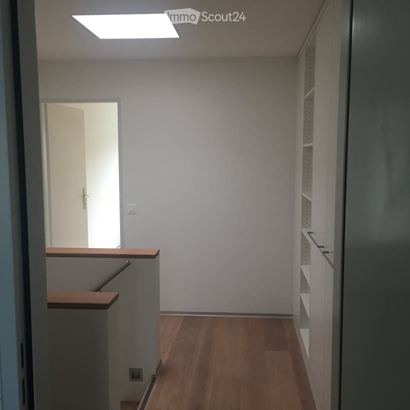 Empty hallway with wooden flooring, white walls, and a staircase leading upwards. A door is visible at the end of the hallway.