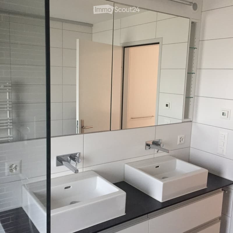 Modern bathroom with two white sinks, chrome faucets, and a large mirror above the vanity.