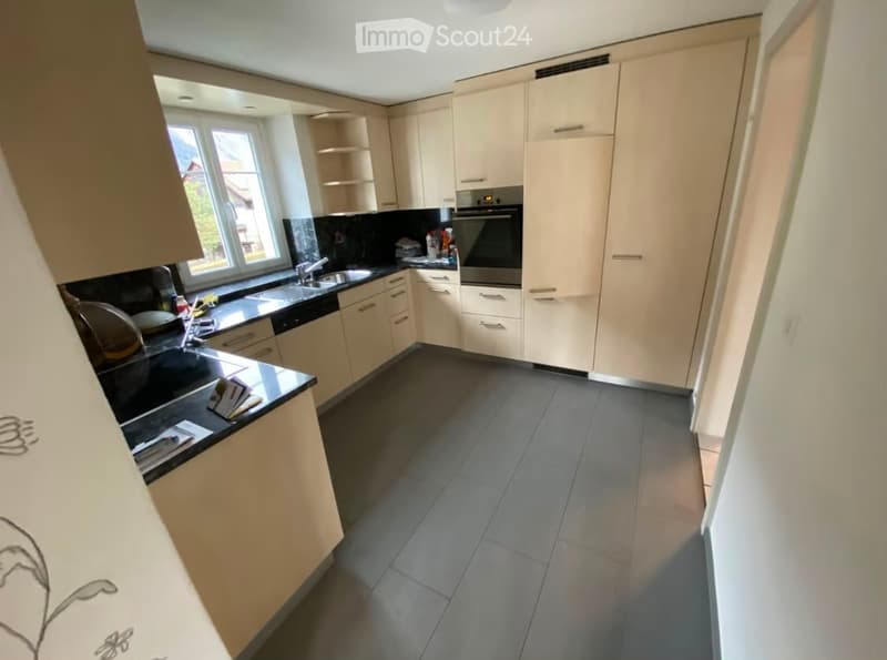 Modern kitchen with light-colored cabinets, black countertops, stainless steel appliances, and a large window providing natural light.
