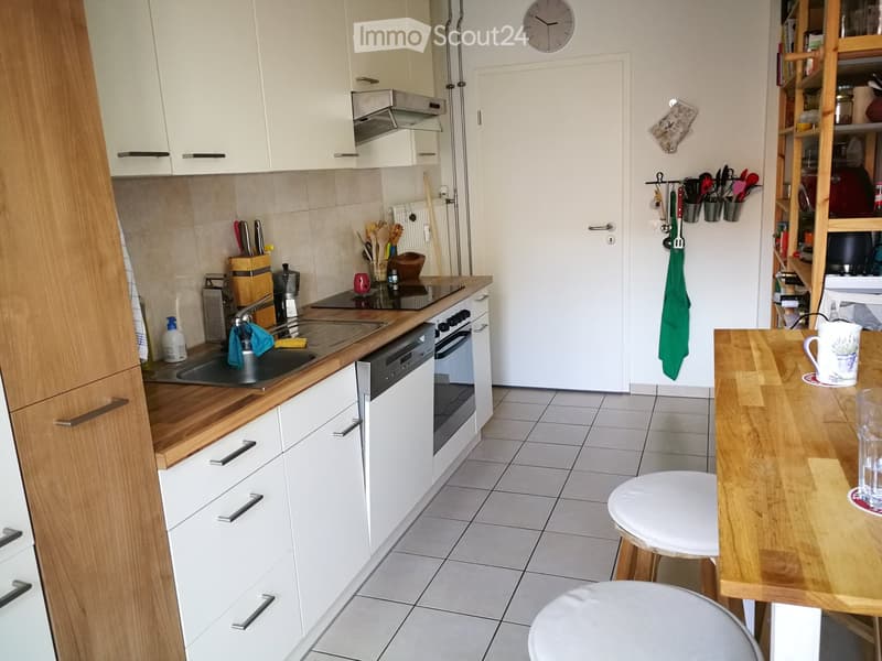 Modern kitchen with white cabinets, wooden countertops, stainless steel appliances, and a small dining area with a table and stools.