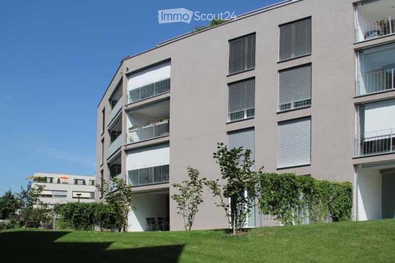 Modern multi-story residential building with balconies, large windows, and a green lawn in front.