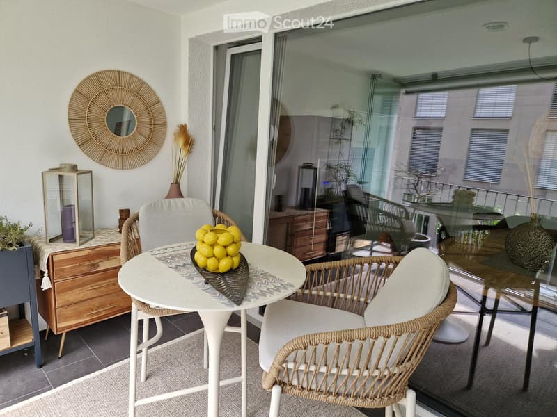 Balcony with a white table, wicker chairs, a vase of lemons, a decorative mirror, and a candle holder.
