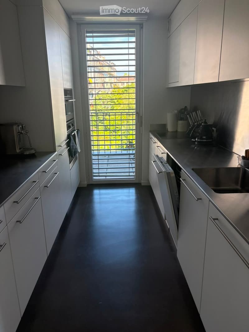 Modern kitchen with white cabinets, stainless steel appliances, and a large window offering a view of greenery outside.