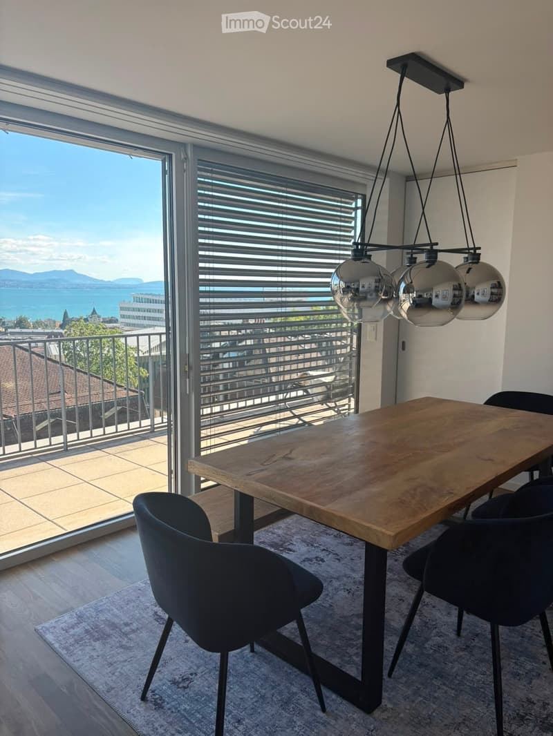 Modern dining area with a wooden table, black chairs, pendant lights, and large windows offering a scenic view.