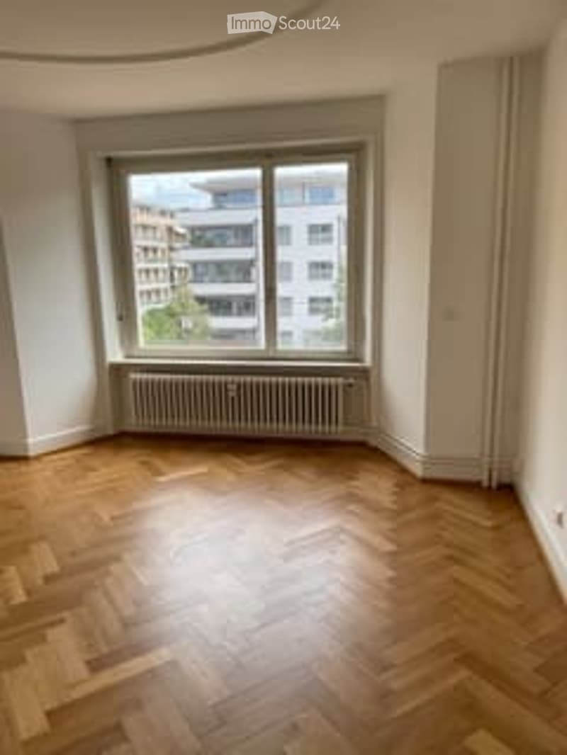 Hardwood floors, white walls, large windows, white door, radiator below the window, unfurnished