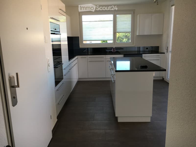 Modern kitchen with white cabinets, black countertops, and a central island. Features an oven, sink, and ample storage space.