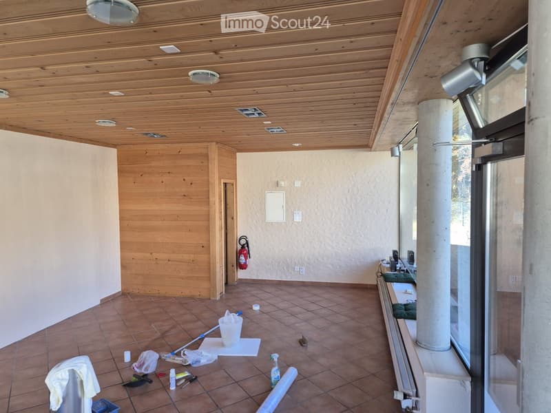 Empty room with wooden ceiling, tiled floor, and large windows. Cleaning supplies and tools are scattered on the floor.