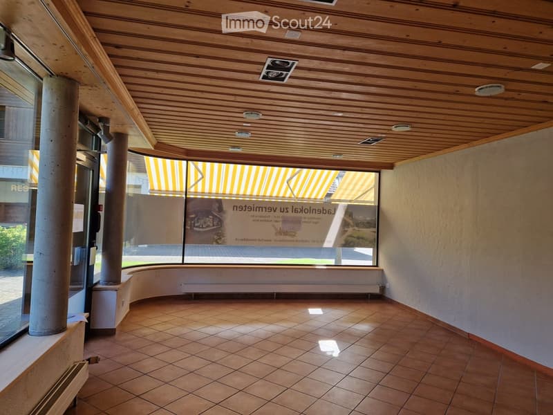 Empty room with tiled floor, large windows, wooden ceiling, and visible structural columns.