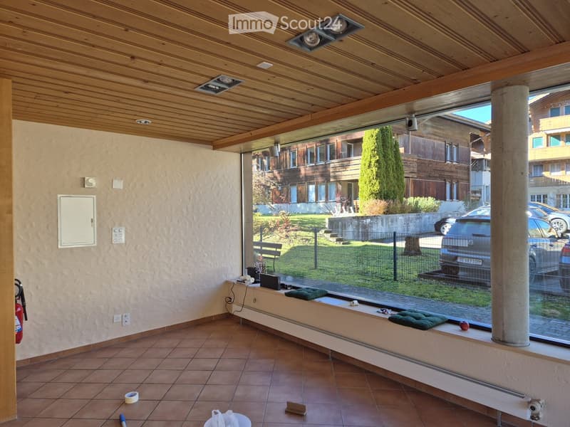 Empty room with tiled floor, wooden ceiling, large window showing outdoor view, and minimal furnishings.