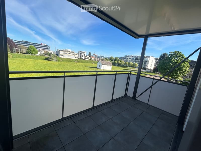 Balcony with tiled floor, metal railing, and a view of a green park and buildings.