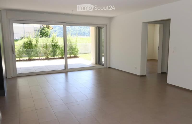 Empty room with tiled flooring, large sliding glass doors leading to an outdoor area, white walls, and an open doorway to another room.