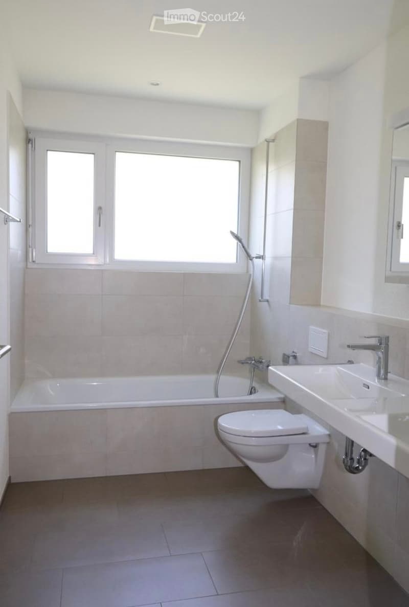 Modern bathroom with a bathtub, toilet, sink, and large window providing natural light.