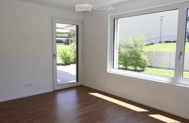 Empty room with white walls, wooden floor, large window, and sliding glass door leading to a patio.