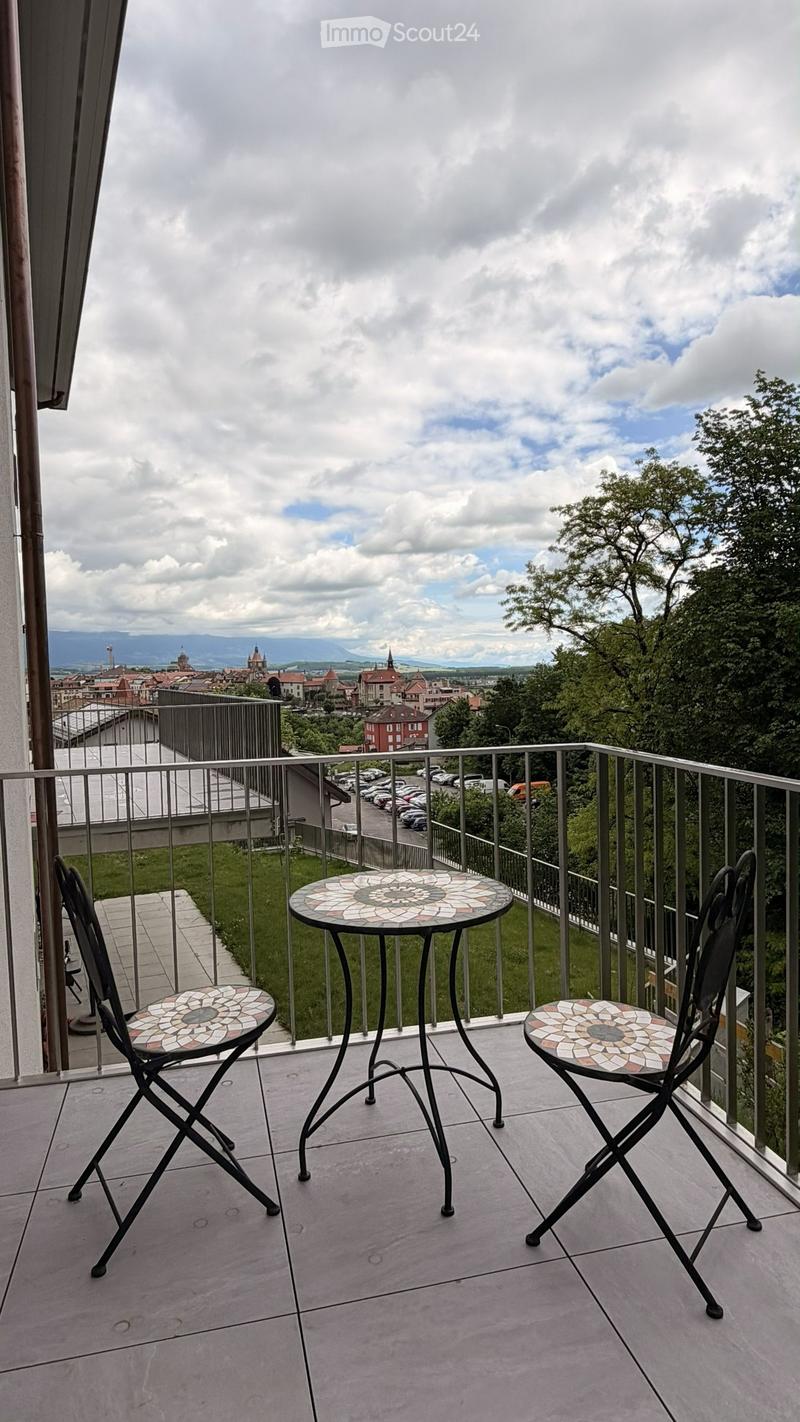 Balcony with a view of a town and mountains, featuring a small round table and two matching chairs with mosaic tile tops.