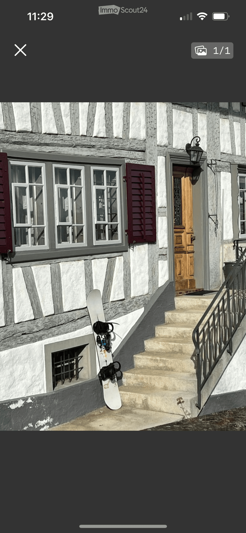 Exterior view of a traditional stone and timber building with a wooden door, steps, and a snowboard leaning against the wall.