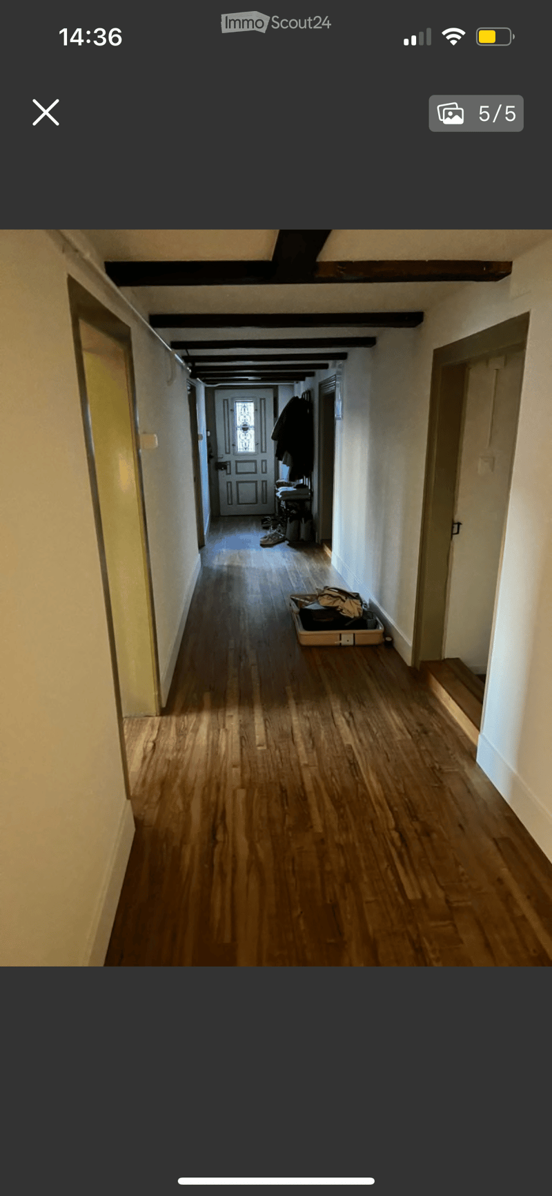 A long, narrow hallway with wooden flooring and white walls, featuring several doors and a staircase leading upwards.