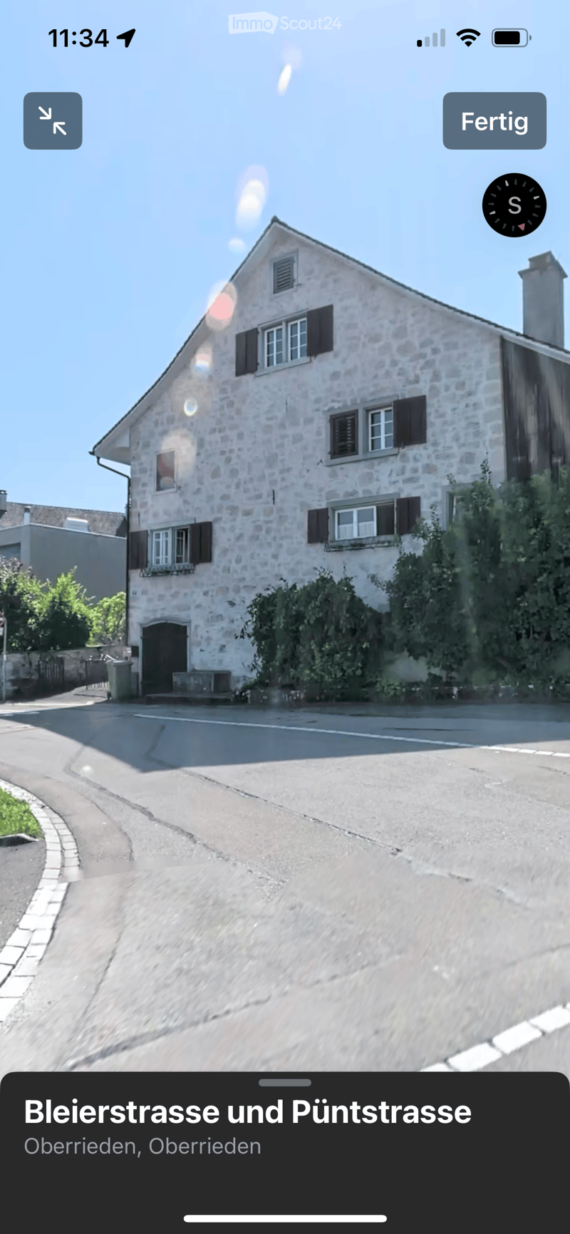 Two-story stone house with multiple windows, shutters, and a small entrance area.