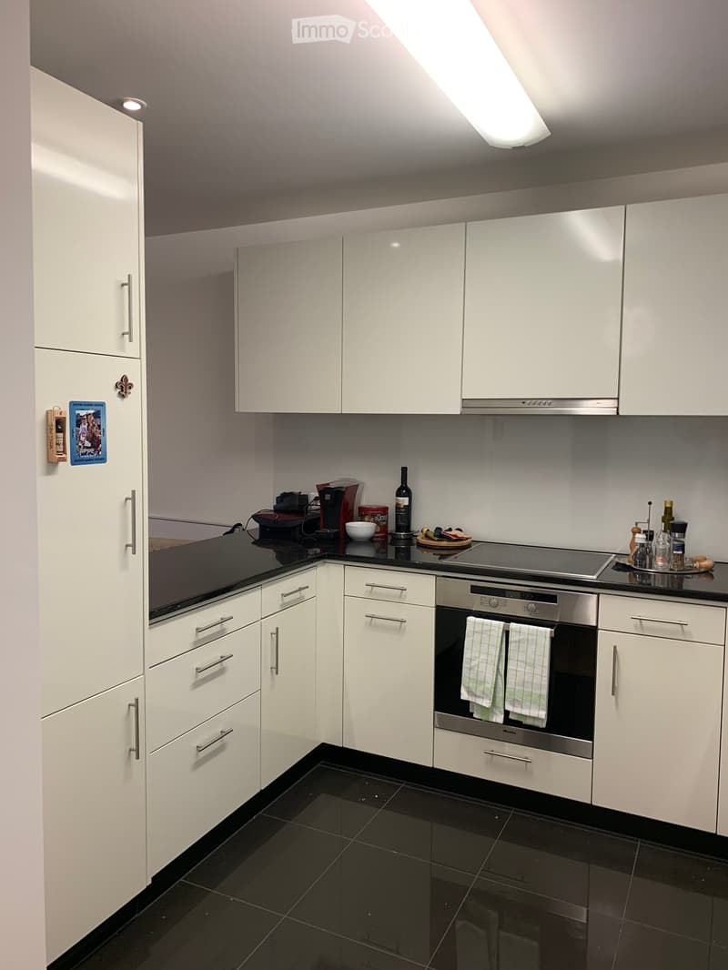 Modern kitchen with white cabinets, black countertops, and stainless steel appliances. Features an oven, coffee maker, and various kitchen items on the counter.