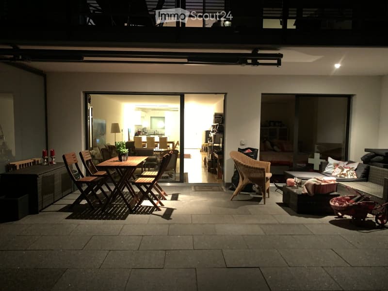 Balcony with a wooden table and chairs, wicker chair, sofa, and view of the interior living space with a kitchen and dining area.