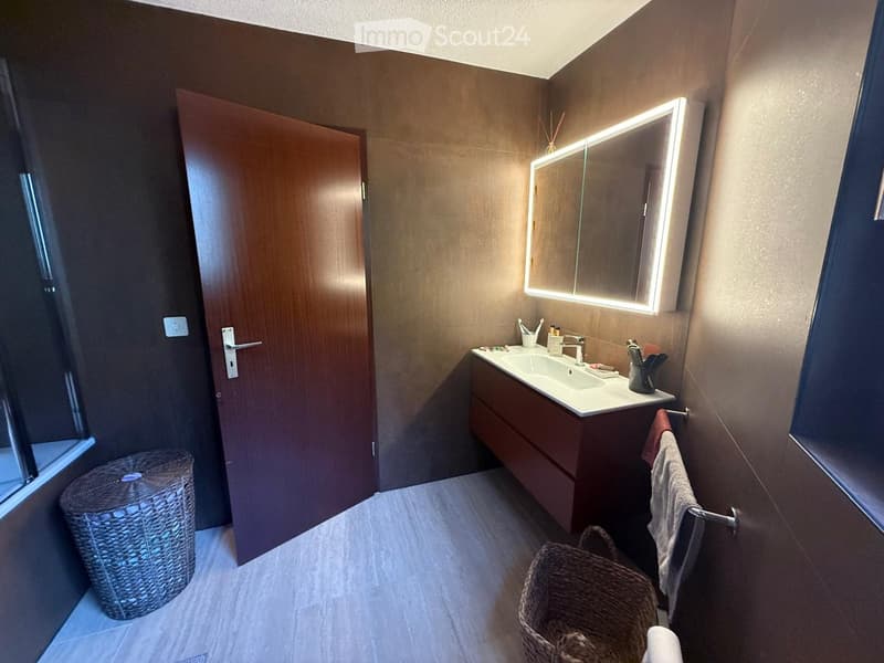 Modern bathroom with a sleek sink, illuminated mirror, and wicker baskets on the floor.