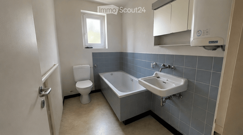 Bathroom with a toilet, bathtub, sink, mirror, and cabinet. Blue tiles on lower walls, white upper walls, and a window providing natural light.