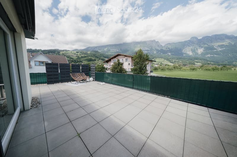 Balcony with tiled floor, green privacy screen, and scenic mountain view in the background.