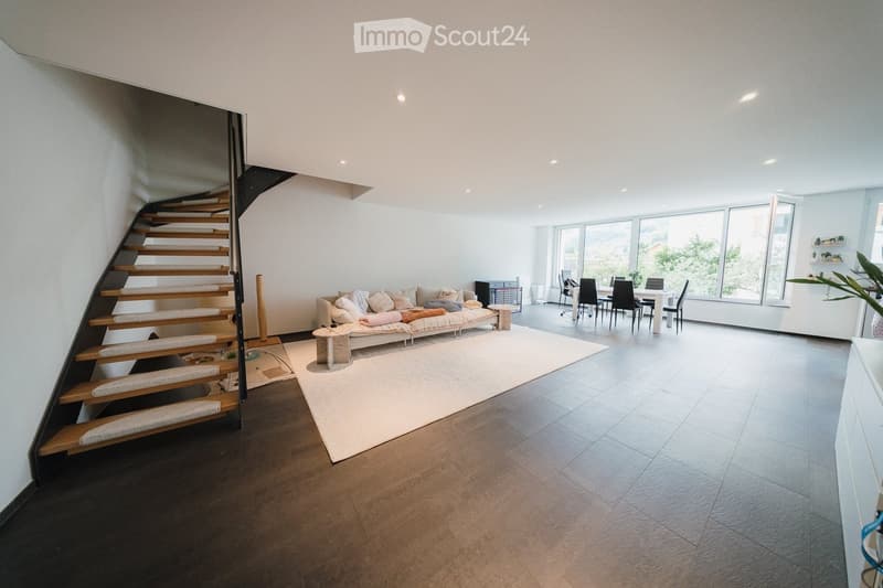 Open-plan living and dining area with a modern sofa, dining table, chairs, and a staircase leading to an upper level.