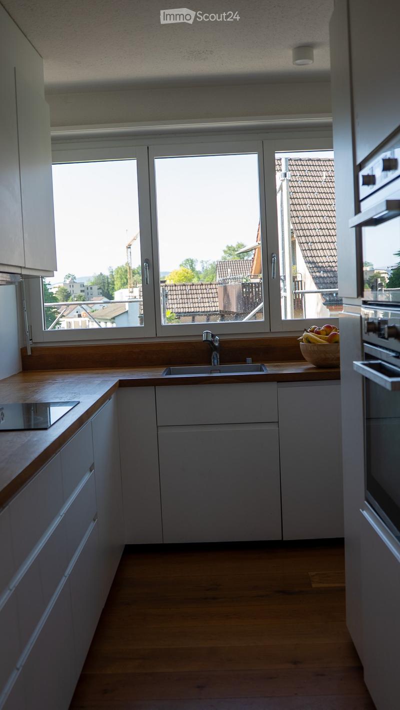 Modern kitchen with white cabinets, wooden countertops, and a large window overlooking a cityscape.