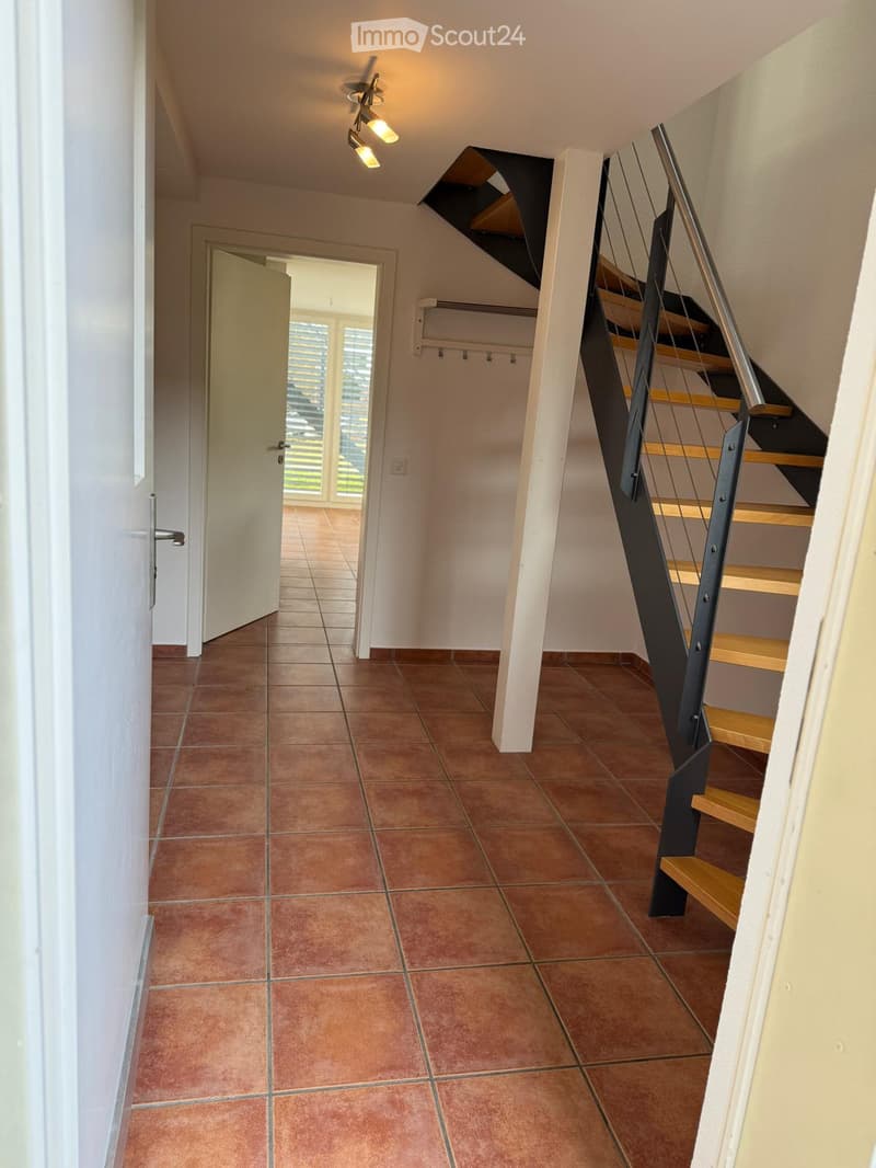 Hallway with terracotta tiled floor, modern staircase with wooden steps and metal railing, white walls, and recessed lighting.
