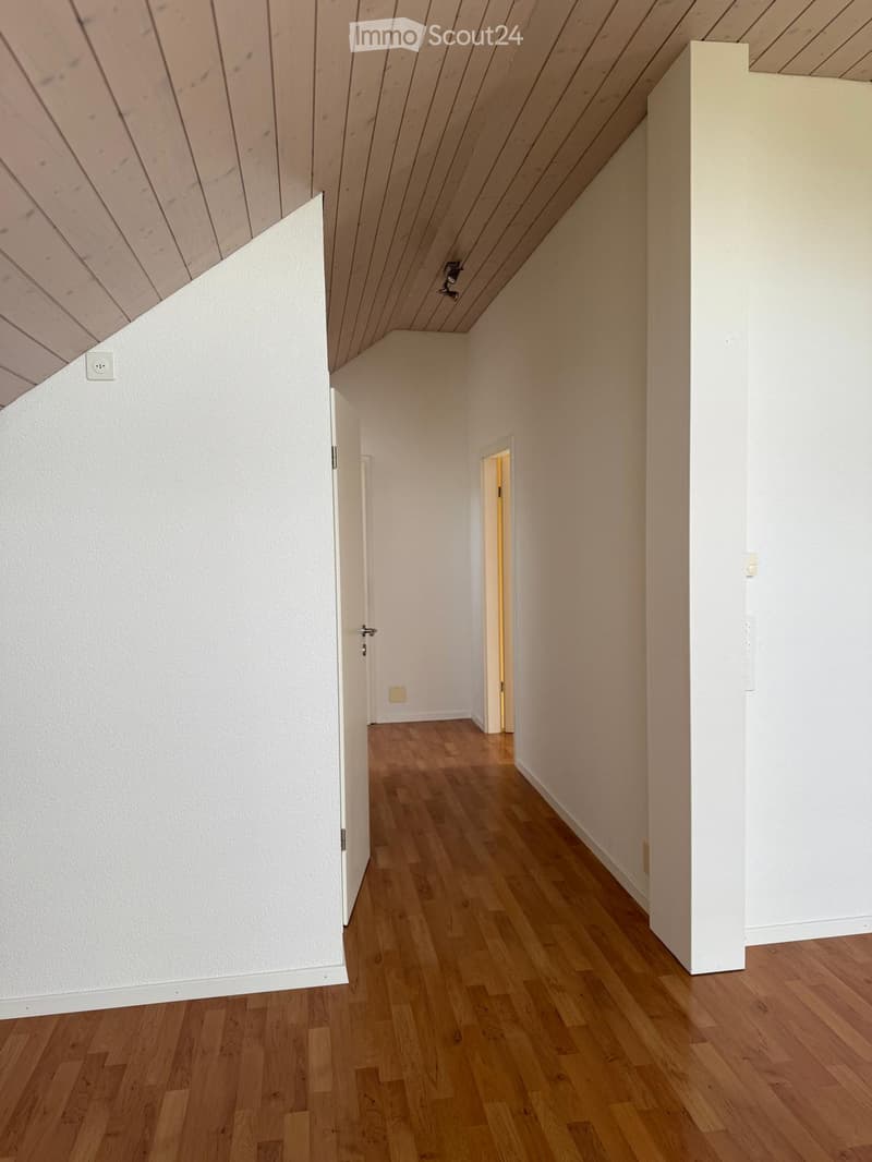 Empty room with white walls, wooden ceiling, hardwood floors, doorway leading to another room, power outlet on wall.
