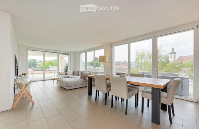 Bright, open living and dining area with large windows, a sofa, a coffee table, a dining table with chairs, and a floor lamp.