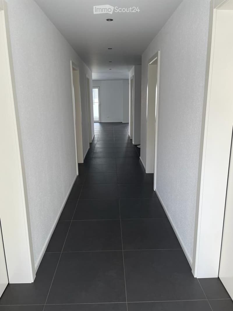 Empty hallway with dark tiled flooring and white walls, featuring several doors and a ceiling light fixture.