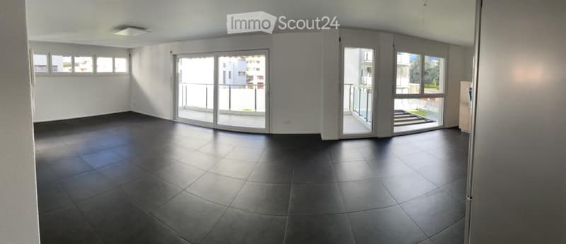 Empty room with dark tiled floor, white walls, large sliding glass doors leading to a balcony, and several windows allowing natural light.