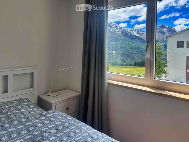 Cozy bedroom with a bed, nightstand, and lamp, featuring large windows with a scenic mountain view.